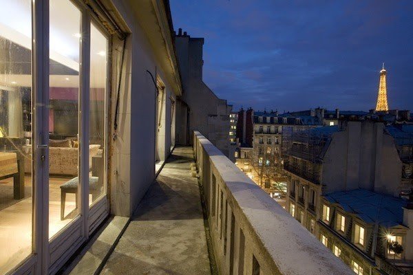 A long balcony overlooking Paris with the illuminated Eiffel Tower in the distance.