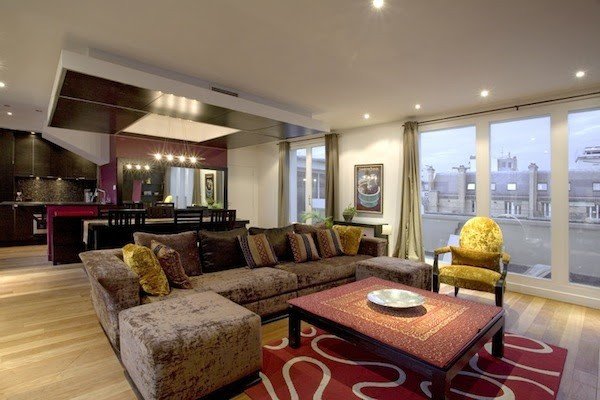 A spacious salon with a corner sofa, patterned rug, and tall balcony doors.